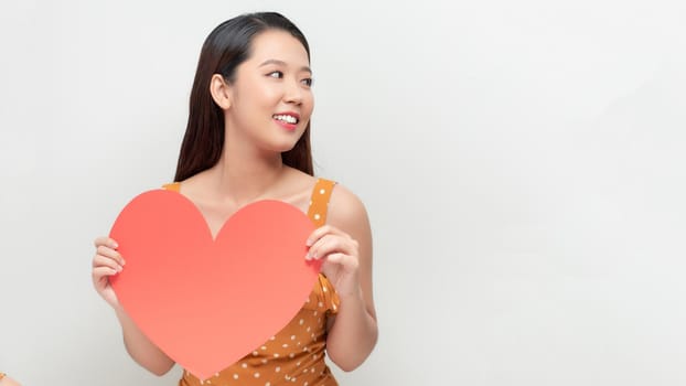 Smiling  asian girl holding big red heart shape, and looking away