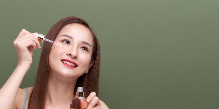  Beauty portrait of smiling young woman girl holding pipette with cosmetic oil or serum near clean face.