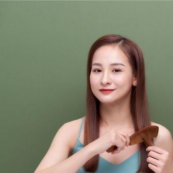 Portrait of cute young woman on green background combing hair.