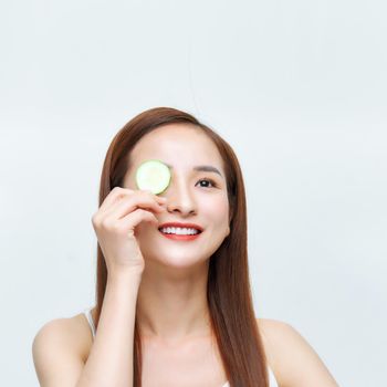 Pretty woman holding cucumber slices over her eyes and laughing