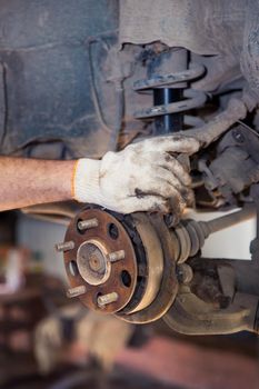 A man's gloved hand holds a rusty car wheel hub. In the garage, a man changes parts on a vehicle. Small business concept, car repair and maintenance service. UHD 4K.