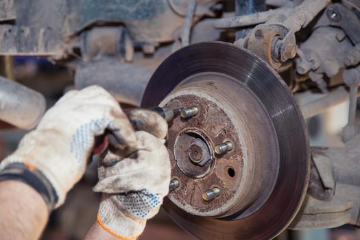 Gloved hands use a screwdriver to tighten the screws on the hub of an old car. In the garage, a man changes parts on a vehicle. Small business concept, car repair and maintenance service. UHD 4K.