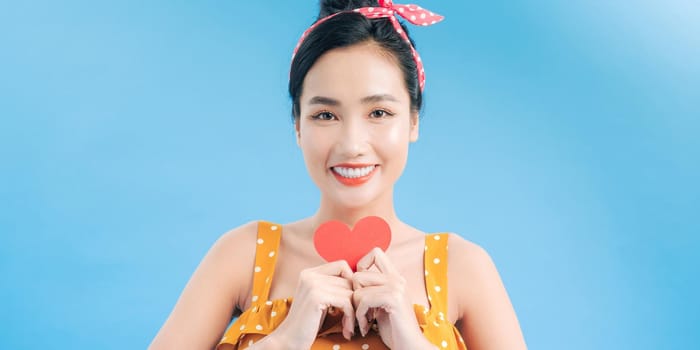 Portrait of pretty smiling woman holding small paper heart in her hands on blue background. Love concept