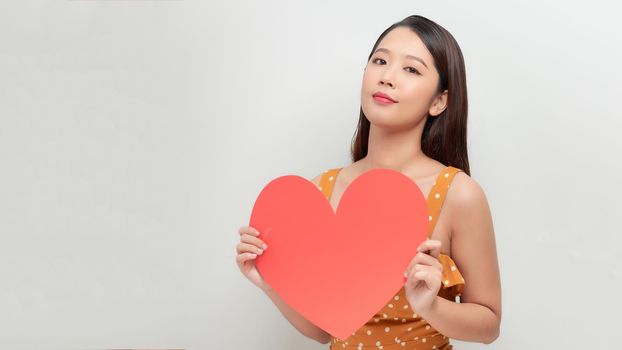 Smiling  asian girl holding big red heart shape, and looking away