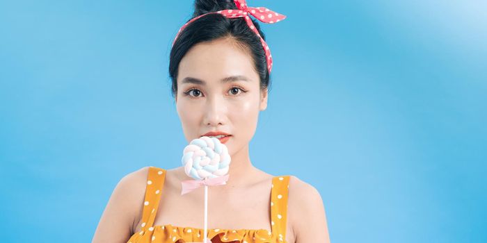 Young asian woman holding a lollipop over blue background with happy expression
