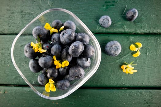 Photographic presentation of a small glass tray filled with ripe blueberries and juicy fruit of the summer season