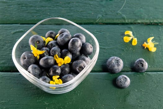 Photographic presentation of a small glass tray filled with ripe blueberries and juicy fruit of the summer season