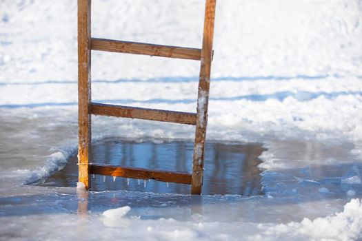 An ice-hole in a winter lake with a wooden ladder. Feast of the baptism of Jesus.