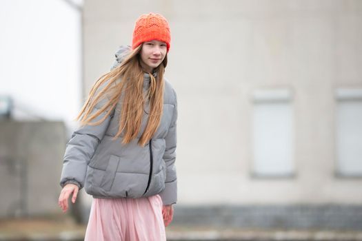 Teenage girl in a knitted hat and warm jacket against the backdrop of the city.