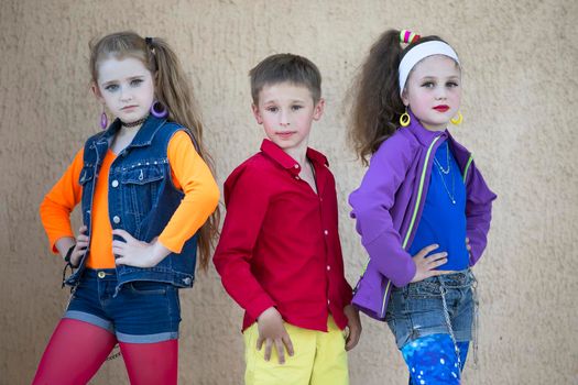 Children pose for a photo shoot. Boy and two little girls models in bright clothes are looking at the camera.