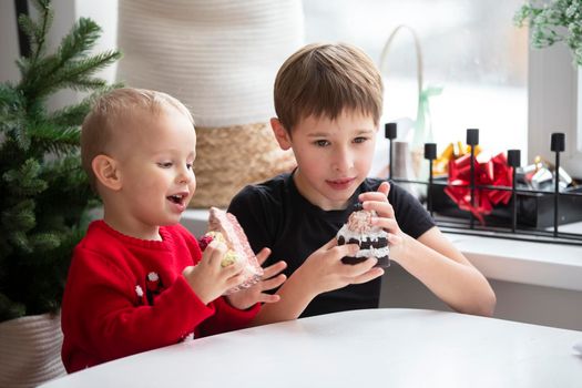 Children eat at Christmas. Two little boys with a piece of cake on the background of a festive Christmas tree.