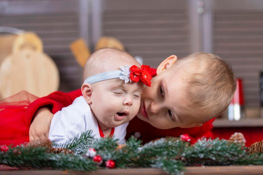 The little brother looks at the yawning newborn sister. Funny kids at christmas time.