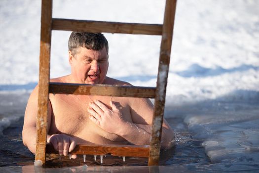 A man plunges into an ice-hole during the winter festival of the baptism of Jesus. A man swims in the ice-hole in winter. Walrus people.