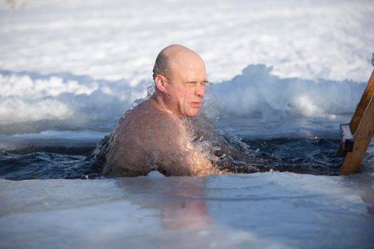 A man plunges into an ice-hole during the winter festival of the baptism of Jesus. A man swims in the ice-hole in winter. Walrus people.