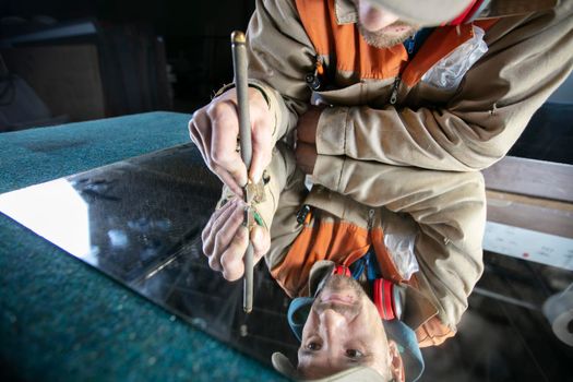 A worker cuts glass with a glass cutter. Furniture manufacturing.