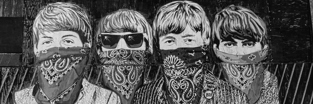 Graffiti by Mr Brainwash on a boarded up building in London showing the Beatles with their mouth covered by bandanna handkerchiefs like outlaw masks.