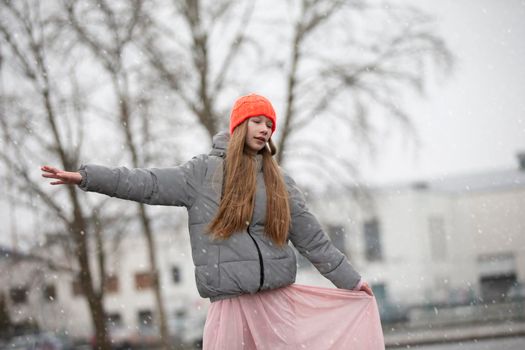Teenage girl in the city in a hat, jacket and pink dress.