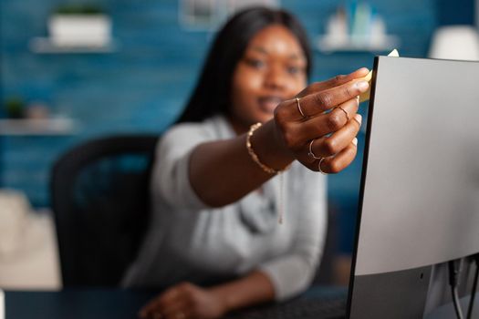 African american student putting stickey notes on computer working remote from home at communication lesson. Woman with dark skin studying math academic lesson using elearning platform