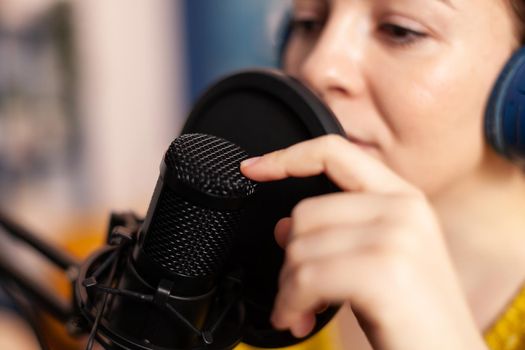 Influencer talking on professional microphone during livestreaming recording vlog in living room. On-air online production internet broadcast show host streaming live content for social media.