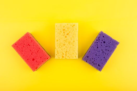 Multicolored red, purple and yellow cleaning and dishwashing sponges on yellow background. Close up, flat lay, dishwashing or house cleaning concept