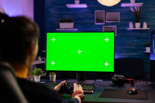 Pro gamer playing virtual videogames on professional powerful computer with green screen display. Cyber Player using pc with mock up chroma isolated desktop streaming shooter games wearing headset