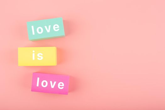 Love is love elegant concept in bright pink colors. Love is love written on multicolored yellow, aqua blue and pink toy cubes on pink background with copy space. Concept of Lgbtq pride social post, tolerance, respect and equal rights