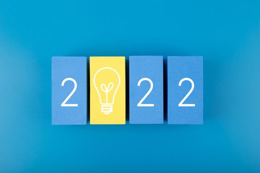 2022 numbers with light bulb on dark blue background. Minimal flat lay composition with blue and yellow toy blocks with written 2022 numbers. Concept of 2022 ideas, technologies and inspirations or start ups
