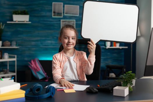 Young student holding blank white board sign for conceptual image at home desk. Smart primary education class lesson pupil learning while using computer and background template