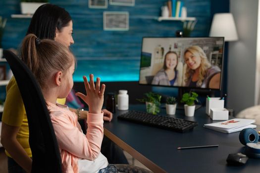 Young child and adult using video call with friends and family while being at home. Mother and daughter on online virtual communication conference computer with cheerful relatives