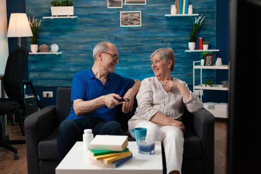 Old couple enjoying retirement at home sitting on sofa watching television. Senior people having fun together with tv movie technology for relaxation entertainment being indoors