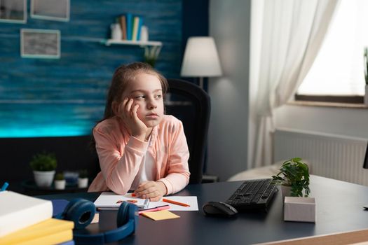 Little girl doing homework feeling bored and sad at home desk. Smart child with overload problem being exhausted from class notes. Overwhelmed from studying and school lesson work