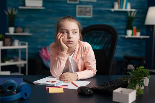 Little girl doing homework feeling bored and sad at home desk. Smart child with overload problem being exhausted from class notes. Overwhelmed from studying and school lesson work