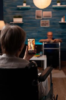 Disabled woman in wheelchair using video call technology on online internet connection smartphone talking to family. Senior people with injury sitting at home with helpful equipment