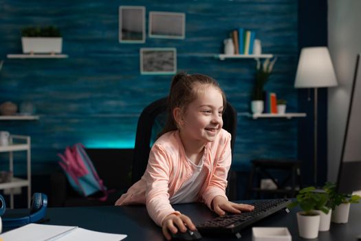 Primary schoolgirl looking at computer monitor for online class lecture on internet connection and technology. Smart caucasian student on digital communication lessons and study meeting