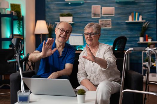 Old married couple using video call online conference technology for modern communication device gadget with family and friends. Retired people sitting at home on laptop with internet