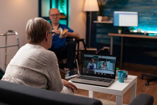 Old grandmother calling doctor in hospital ward clinic to check healthcare diagnosis on video call conference. Woman talking to medic about treatment for niece while man sits in wheelchair