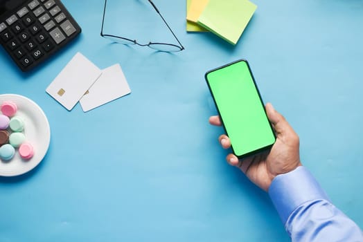 Top view of man hand holding smart phone with empty screen on office desk .