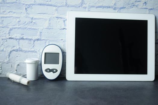 top view of digital tablet, pills and diabetic measurement tool on table.