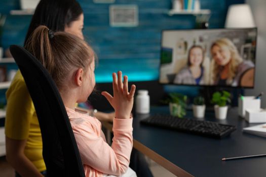 Caucasian family waving at webcam using video call technology online conference communication on internet. Mother and little kid talking to friends on modern computer monitor website app