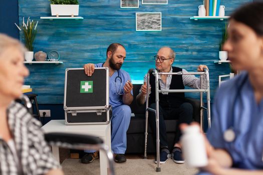 Social assistant discussing healthcare medication with elderly disabled pensioner man during nursing services in retirement home. Support worker prescribing pills treatment. Social helper