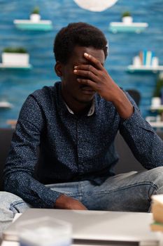 Portrait of stressed, pensive african american man looking out the window thinking about business problems. Adult man in living room working from home office desk. Serious black person