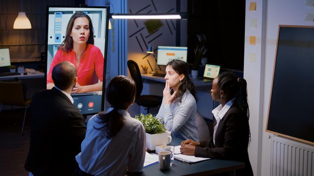 Workaholics diverse multi-ethnic teamwork having online videocall conference meeting overworking at financial strategy in office room late at night. Focused teamwork discussing company ideas in evening