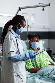 African american patient sitting in bed while doctor check healthcare and disease development in hospital ward at medical clinic. Specialist consulting young adult for medicine and treatment