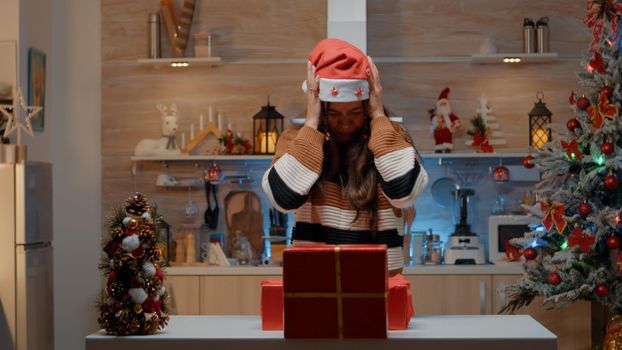 Young person dropping gift boxes on kitchen floor at festive home decorated for christmas. Woman preparing to give presents to friends and family at seasonal holiday party gathering