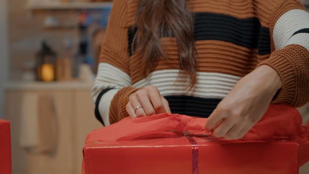 Close up of woman wrapping bow on gift for friends in festive kitchen at home. Happy person using present paper and boxes preparing for christmas eve dinner winter celebration