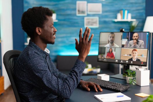 Black man waving to colleagues on video call chat using online internet and webcam communication. Remote worker working from home keeping distance while using technology and computer