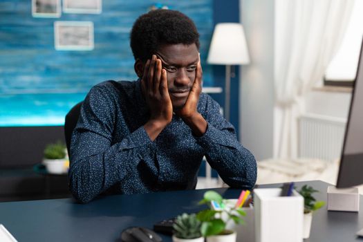 African american man having big headache from stress while rubbing his temples. Tired suffering black guy from working on assignment at office. Overwhelmed unhappy business person