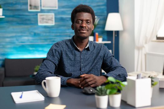 African american man freelancer smiling to camera, young person in modern flat apartment working from home using computer. Black businessman doing work tasks