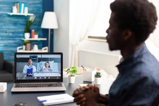 Father on online video call via laptop, talking with doctor from hospital ward about child healthcare, using internet telemedicine app and technology consultation for treatment and diagnose