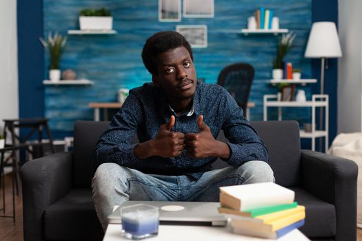 Portrait of thoughtful african american man looking out the window, thinking about workplace business problems. Black adult sitting in living room on couch working from home office